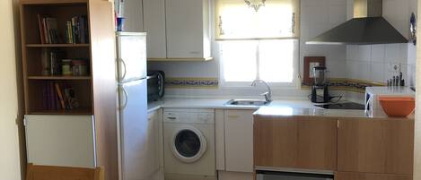 A compact kitchen with a washing machine, a sink, and a dining area with a table and chairs.