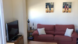 A living room with a television on a wooden stand, a red sofa with two pillows, and two paintings on the wall. - Attic Lo Pagan in Mar Menor (San Pedro del Pinatar)