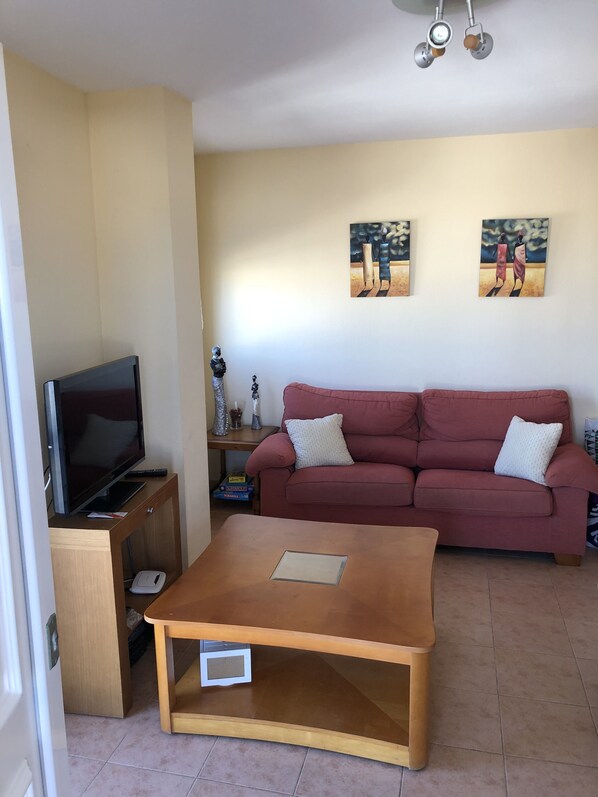 A living room with a television on a wooden stand, a red sofa with two pillows, and two paintings on the wall. - Attic Lo Pagan in Mar Menor (San Pedro del Pinatar)