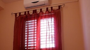 A room with a bed, a window with red curtains, and an air conditioning unit above the window.