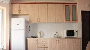 A kitchen with light wooden cabinets, a white refrigerator, a kettle, a microwave, and a sink.