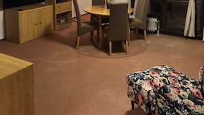 Ett mysigt vardagsrum med ett träpanelat tak, en tv, ett träskåp, ett matbord med stolar och en blommig pall.