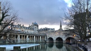 A historic stone bridge over a calm river, with buildings and a church tower in the background. - The King's Meadery (Bath)