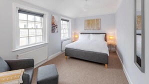 A bedroom with a large bed, two bedside tables with lamps, a window with blinds, and a radiator. - The King's Meadery (Bath)