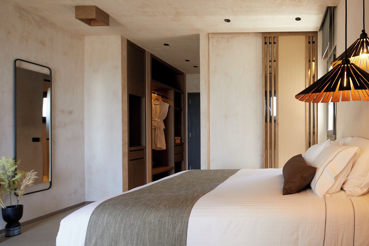 Un dormitorio moderno con una cama grande, una lámpara colgante, un espejo y un vestidor.
