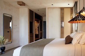 Un dormitorio moderno con una cama grande, una lámpara colgante, un espejo y un vestidor.