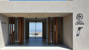 Une entrée d’hôtel moderne avec un comptoir de réception portant l’inscription « RÉCEPTION » et une vue sur l’océan à travers les portes vitrées.
