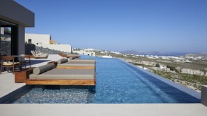 Une piscine à débordement située sur le toit, avec des chaises longues et un espace repas, offrant une vue sur un paysage côtier.