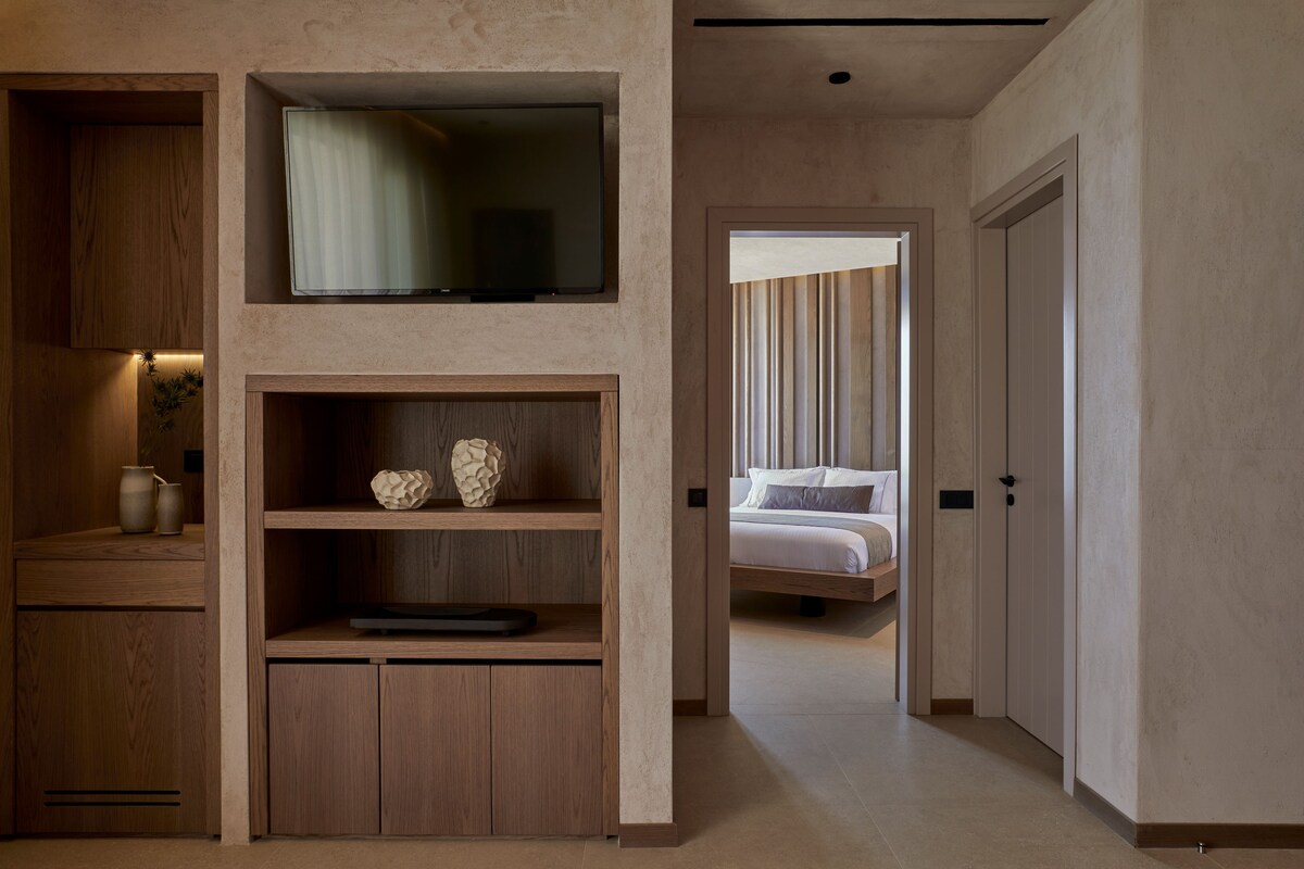 Habitación de hotel moderna con un armario de madera, televisor de pantalla plana, cama con vistas al exterior y una puerta que da a otra habitación.
