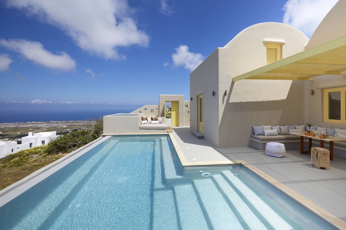Une piscine sur le toit offrant une vue dégagée sur l’océan, un espace détente avec des coussins et une table en bois.
