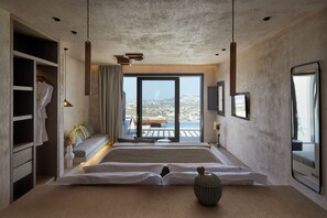 A modern bedroom with a large bed, a wardrobe, a view of the sea, and a balcony.