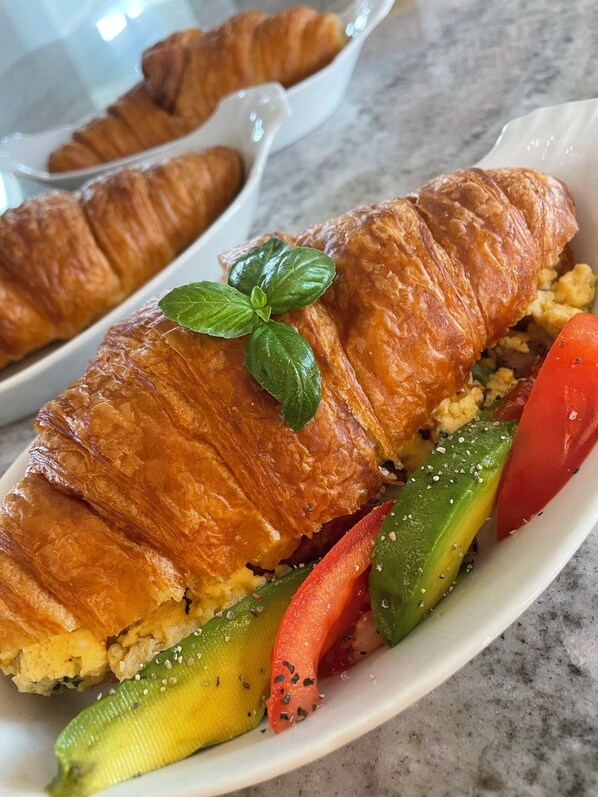 Un plat amb un croissant, verdures i una fulla de bàsil.