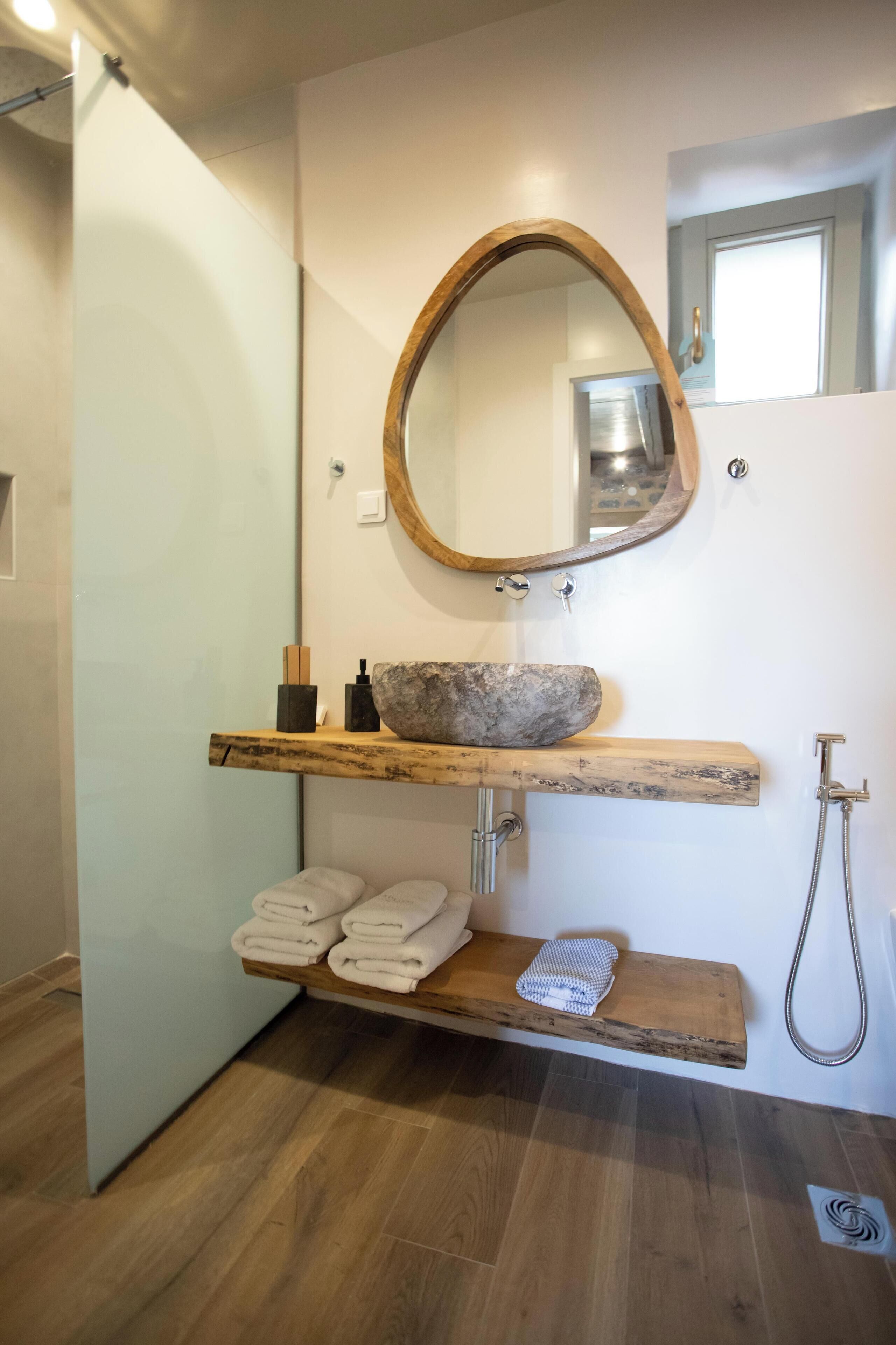 Un baño con un estante de madera con toallas, un lavabo de piedra y un espejo con marco de madera.