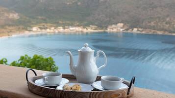 A tray with a teapot, cups, and a biscuit on a balcony overlooking a body of water.