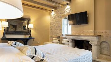 A bedroom with a stone wall, a fireplace, a bed with white bedding, and a mounted TV.