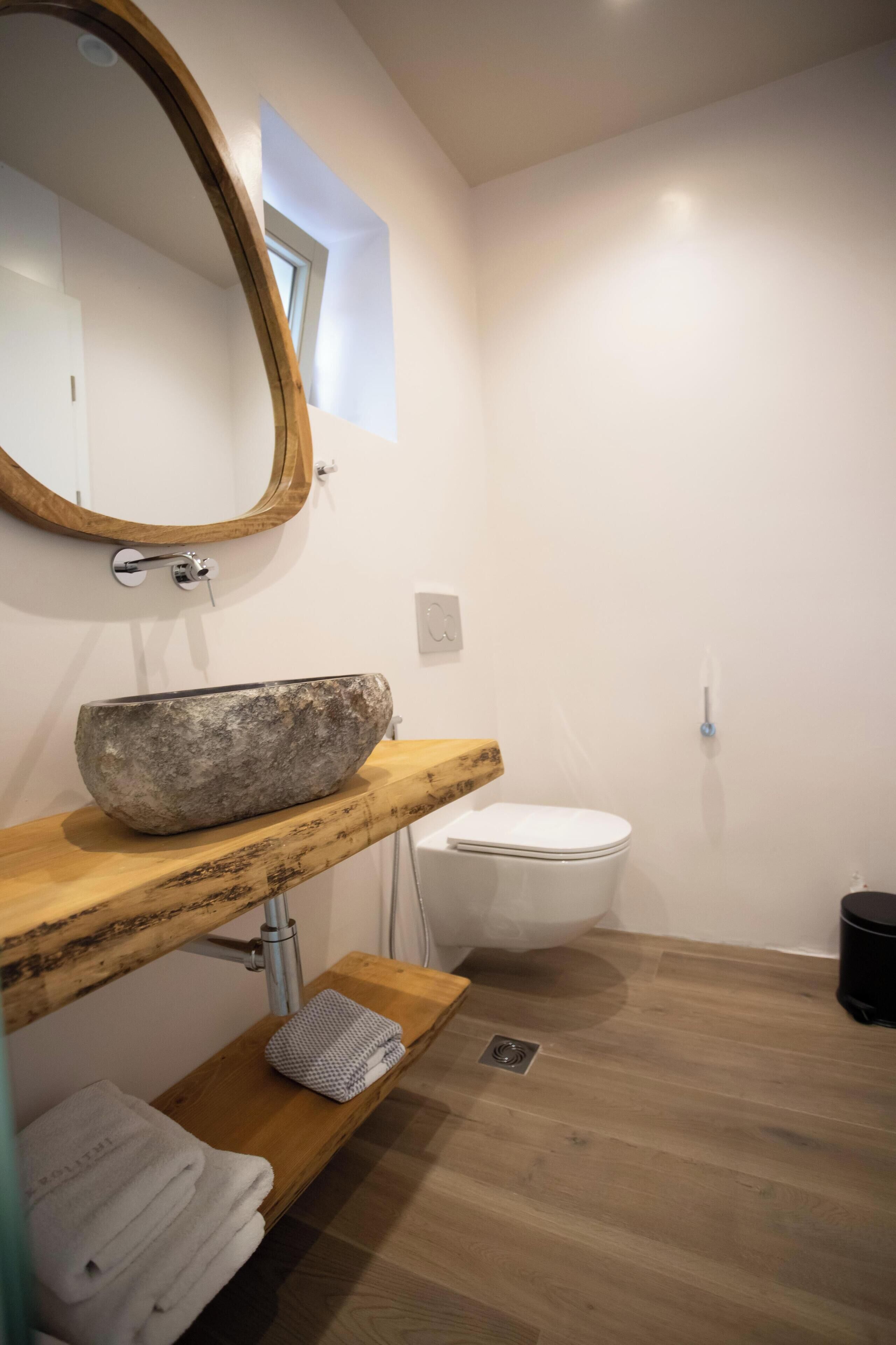 Un baño con tocador de madera, lavabo de piedra, inodoro blanco y espejo con marco de madera.