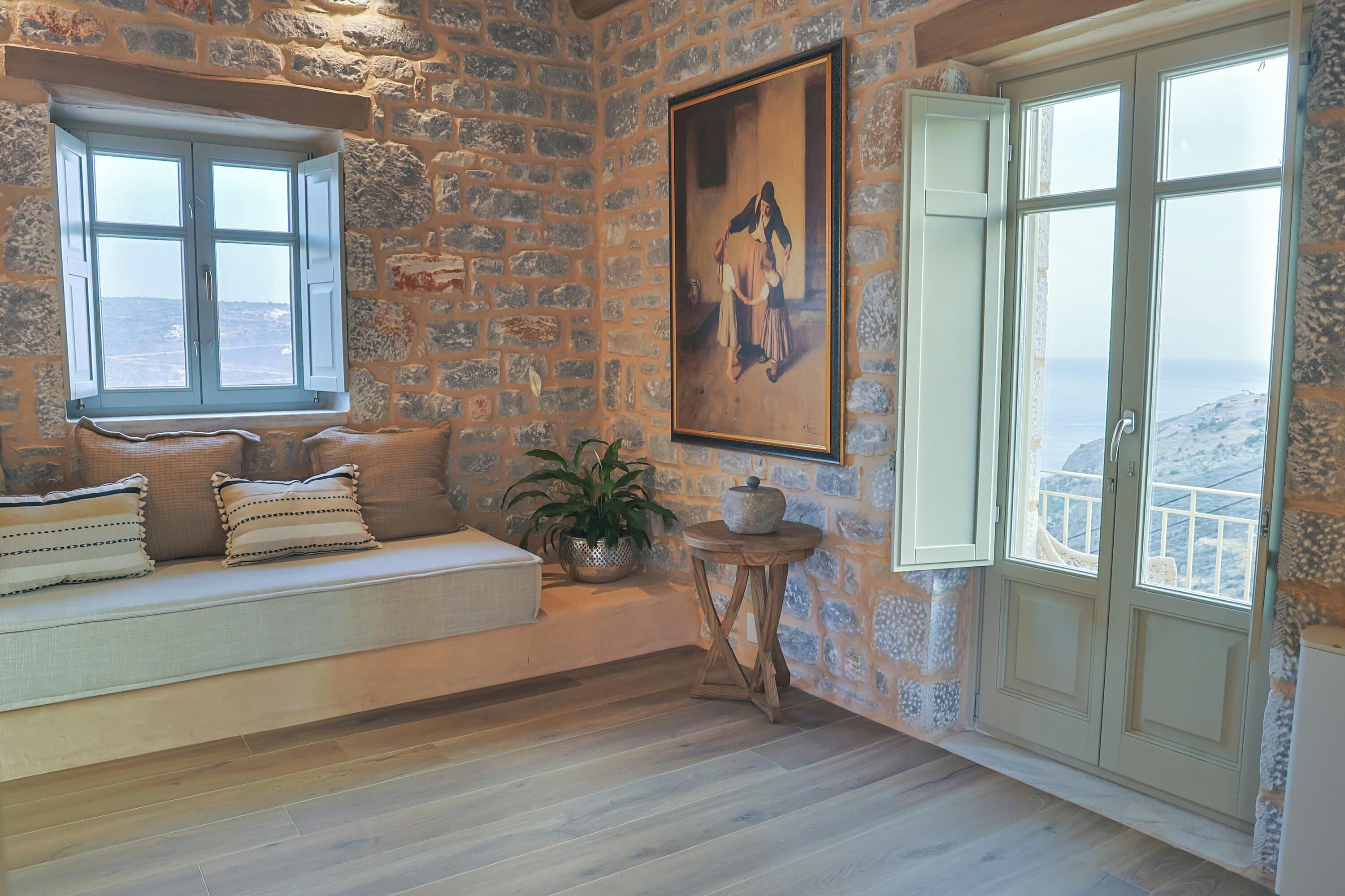 Habitació de paredes de pedra amb una banca, una finestra gran i un quadre.