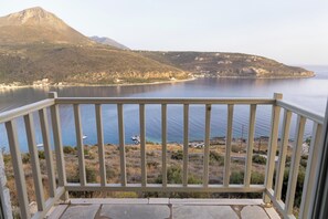 A balcony with a view of a calm sea, a distant mountain, and a small boat. - Akrolithi Guesthouse (East Mani)