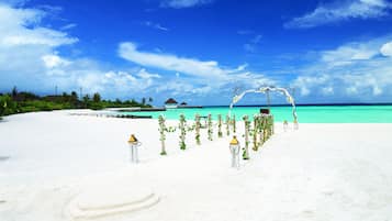 Montaje para una boda en la playa con un sendero de arena blanca, un arco floral y vistas al océano turquesa.