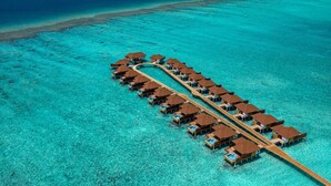 An overwater bungalows with a wooden walkway connecting them, set in clear turquoise waters.
