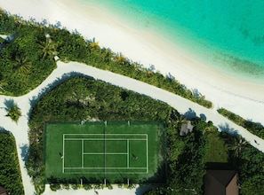 An aerial view of a beach with a tennis court surrounded by lush greenery and white sand.