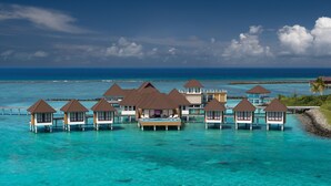 Overwater bungalows with private pools, connected by walkways, set against a clear blue sea and sky.