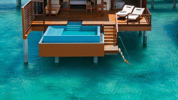 An overwater bungalow with a pool, wooden deck, and lounge chairs.