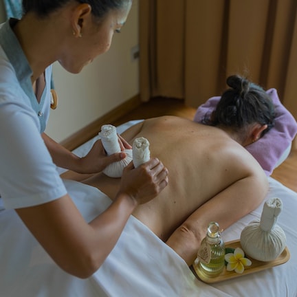 A massage therapy session in a room with a bed, a massage table, and a window with curtains.