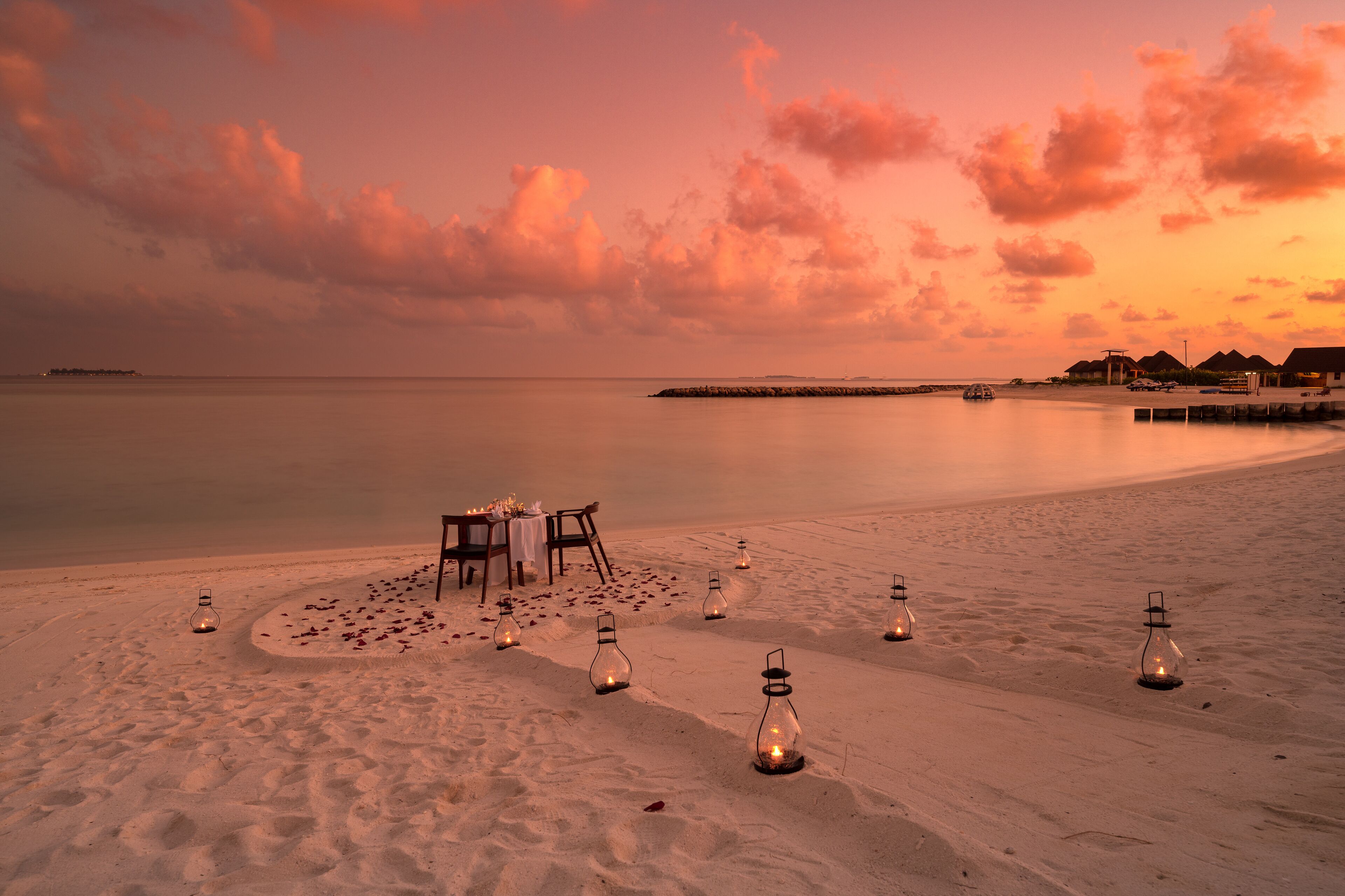 A beach setting with a table and chairs set up for dining, surrounded by lanterns.
