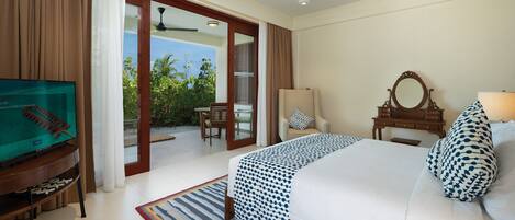 A hotel room with a bed, a television, a ceiling fan, a window with curtains, a chair, and a view of greenery outside.