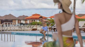 A swimming pool with a clear blue water surface, surrounded by lounge chairs and umbrellas.