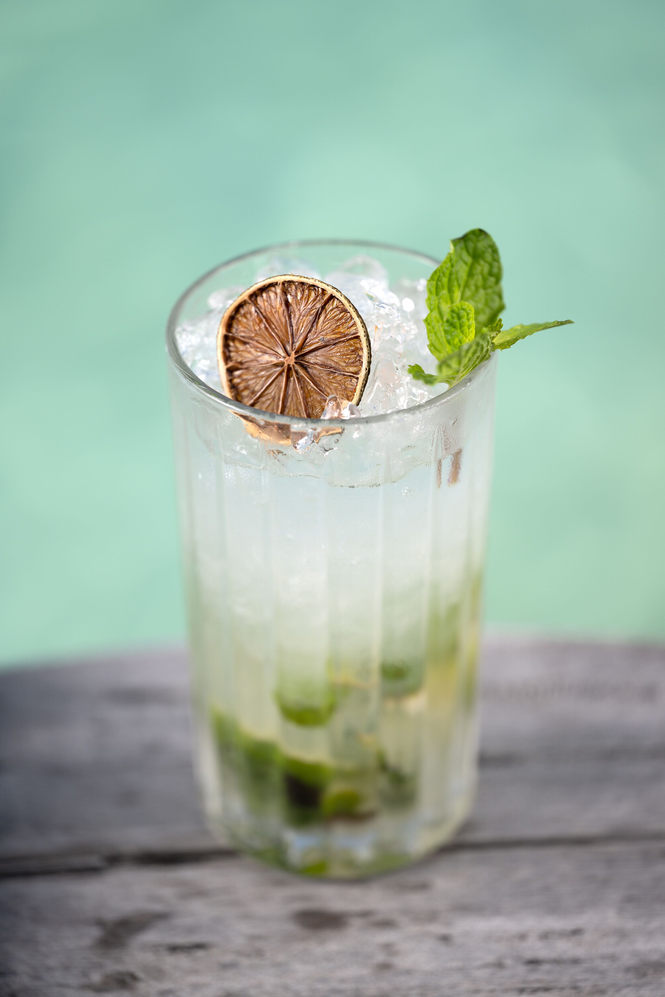 Un vaso con hielo, hojas de menta y una rodaja de naranja deshidratada.