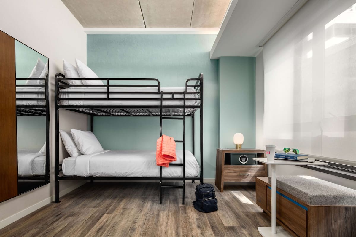 A bunk bed room with a desk, a chair, and a small table with a lamp.