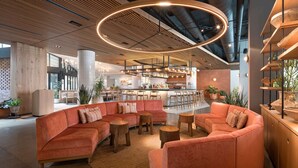 A modern lounge area with a curved orange sofa, wooden tables, and a circular light fixture. - Motto by Hilton Philadelphia Rittenhouse Square (Philadelphia)