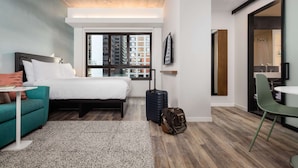 A modern hotel room with a bed, a small table, a sofa, a suitcase, and a bathroom visible through an open door. - Motto by Hilton Philadelphia Rittenhouse Square (Philadelphia)