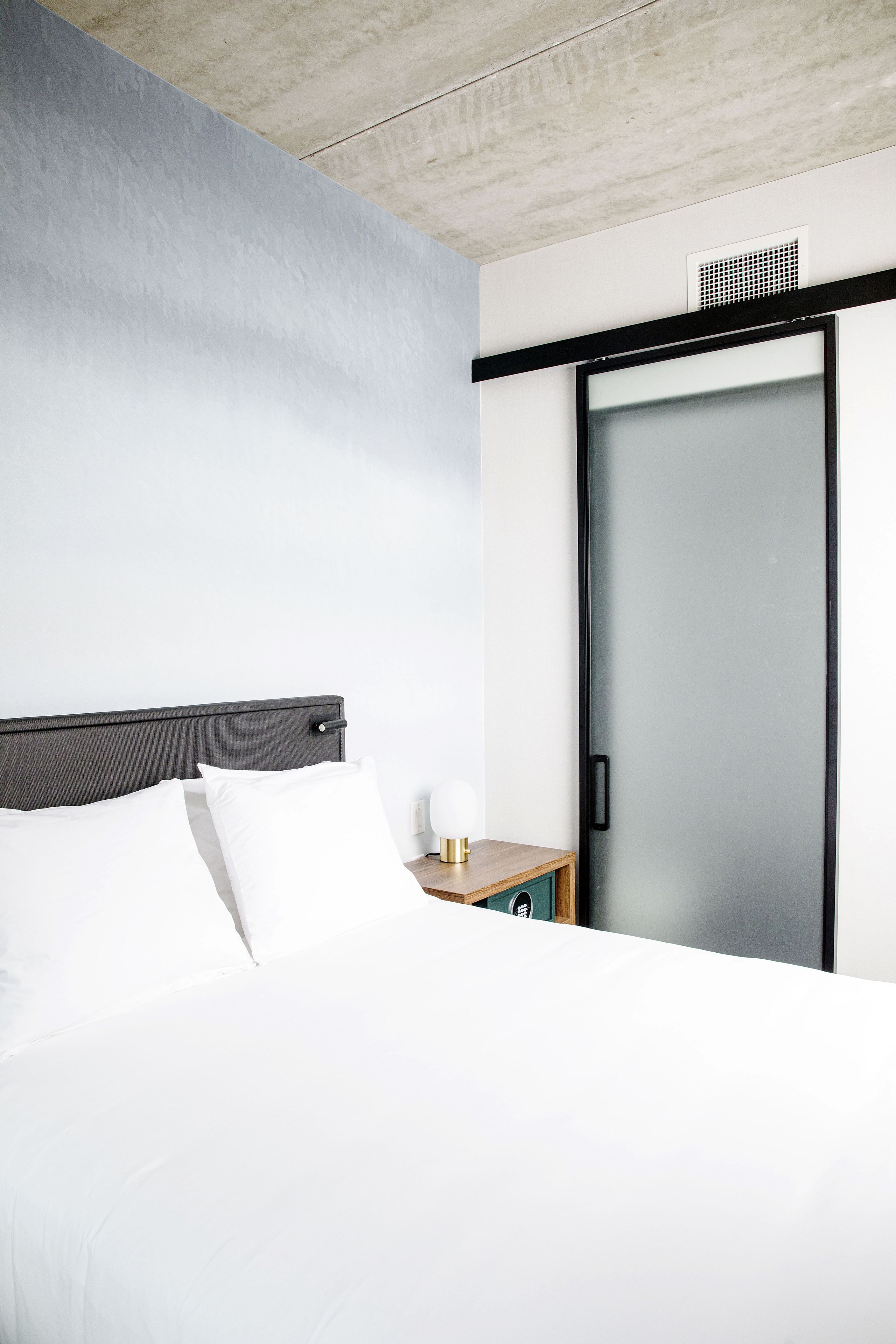 Habitación de hotel con cama, mesita de noche, lámpara y puerta corrediza.