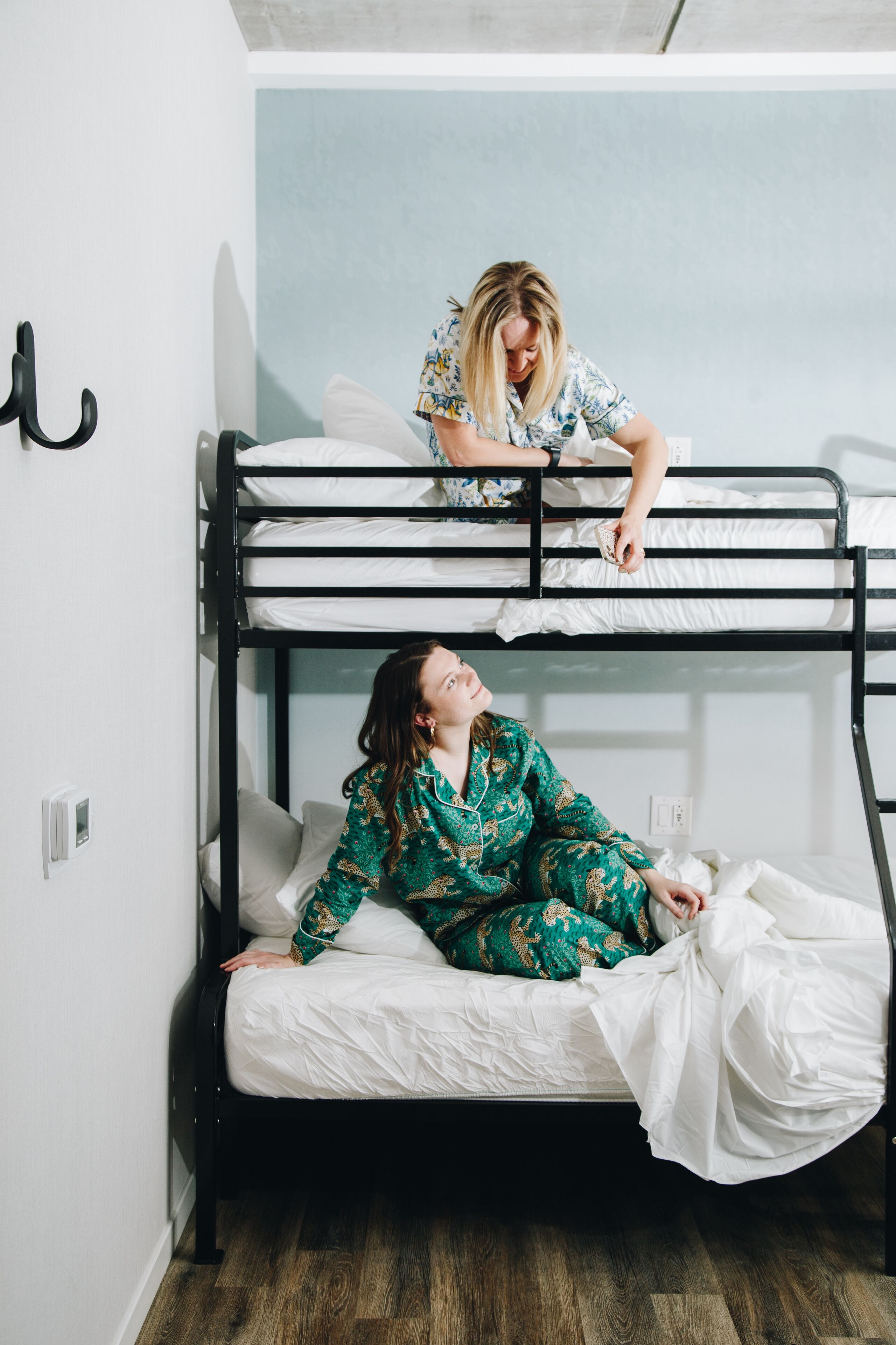 A bunk bed room with a person standing on the top bunk and another person lying on the bottom bunk.