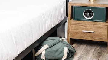 Uma cama bem arrumada com lençóis brancos, uma mesa de cabeceira com uma gaveta verde e um par de tênis no chão.