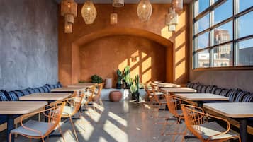 A modern cafe with wooden tables and orange chairs, large windows, and hanging wicker lamps.