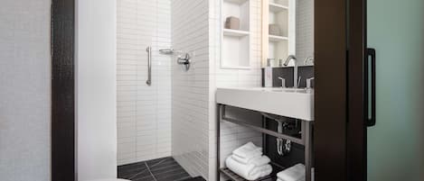 A modern bathroom with a white toilet, a shower with a handheld showerhead, a vanity with a mirror and shelves, and a towel rack.