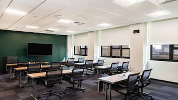 Un salón de conferencias con varias mesas y sillas, una pantalla grande y ventanas con vistas a la ciudad.