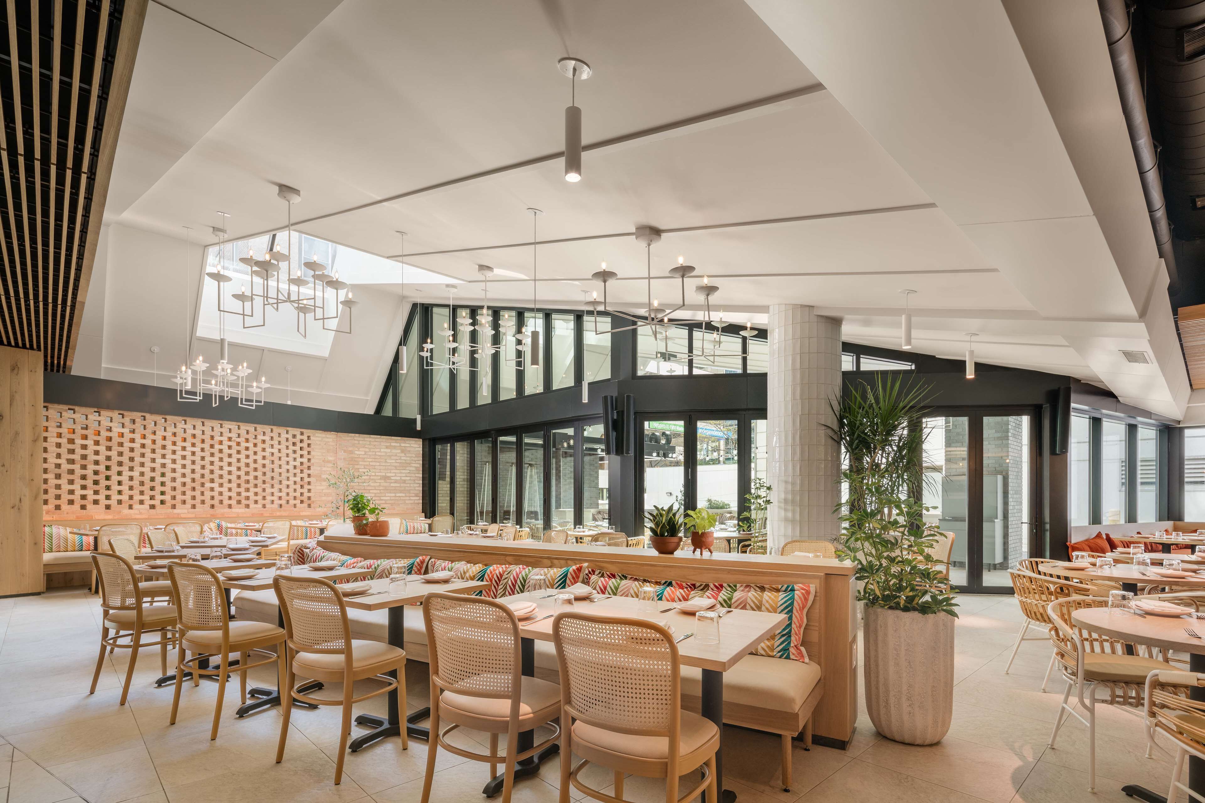 En moderne restaurant med høje lofter, store vinduer og forskellige siddepladser, herunder borde og båse.