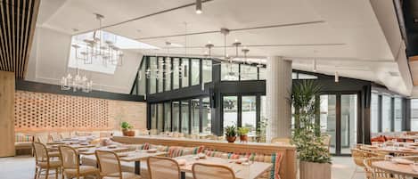 Un restaurante moderno con techos altos, amplios ventanales y diferentes opciones de asientos, incluyendo mesas y cabinas.