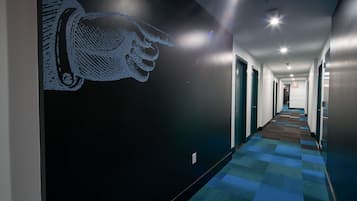 A hotel hallway with a patterned carpet, a wall mural, and doors leading to rooms.
