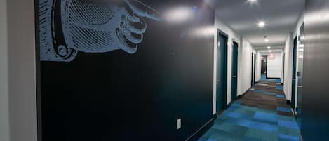Un pasillo de hotel con alfombra estampada, un mural en la pared y puertas que dan a las habitaciones.