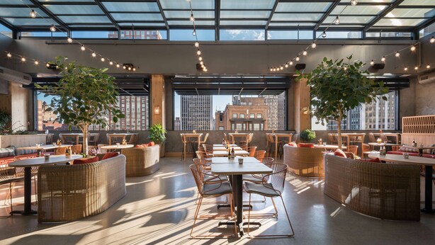 A spacious rooftop dining area with high ceilings, large windows, and string lights. - Motto by Hilton Philadelphia Rittenhouse Square (Philadelphia)