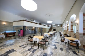 Ein geräumiger Essbereich mit mehreren Tischen und Stühlen, einer Buffetstation und einer Treppe zu einer oberen Ebene.
