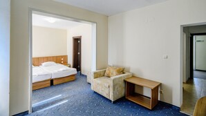 A hotel room with a bed, a sofa, a small table, and a door leading to another room. - International House of Journalists (Varna)