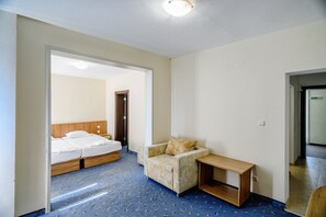 A hotel room with a bed, a sofa, a small table, and a door leading to another room. - International House of Journalists (Varna)