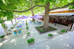 An outdoor seating area with tables and chairs, surrounded by trees and planters. - International House of Journalists (Varna)